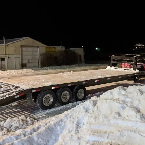 Three-axle gooseneck flatbed hitched to the truck on a snow-packed Red Deer street at night, load strapped down at the nose