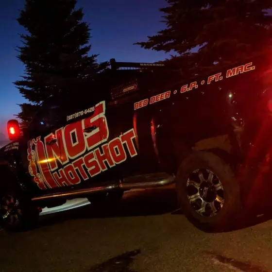 Wrapped truck under evening light, the red NOS Hotshot logo glowing on the black door panel